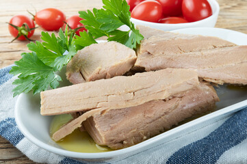 Tuna fillets in olive oil with parsley and cherry tomatoes on wooden background.