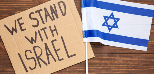 Flag and cardboard with text WE STAND WITH ISRAEL on wooden background