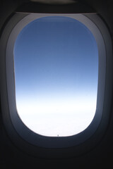 View through a small window of an airplane in which you can see the blue of the sky