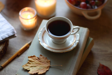 Cup of tea or coffee, plate with desserts, dried oranges, bowl of grapes, scented candles, vintage books, pumpkins and autumn leaves on the table. Autumnal hygge. Selective focus.
