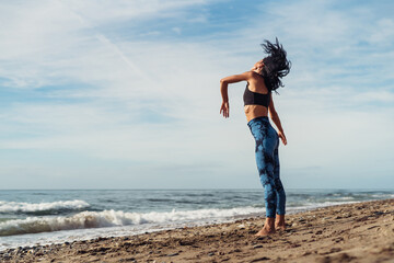 A beautiful brunette girl is dancing on the beach by the sea on the sand