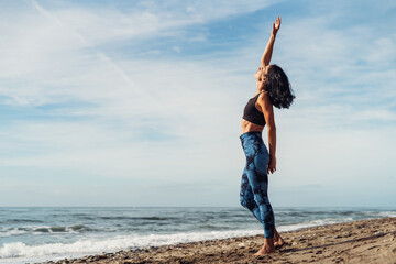 A beautiful brunette girl is dancing on the beach by the sea on the sand
