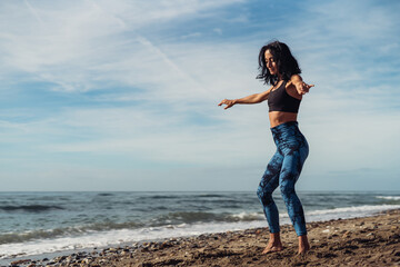 A beautiful brunette girl is dancing on the beach by the sea on the sand