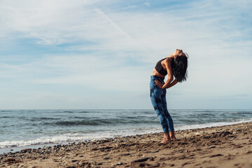 A beautiful brunette girl is dancing on the beach by the sea on the sand
