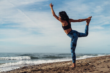 A beautiful brunette girl is dancing on the beach by the sea on the sand