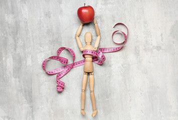 Composition with wooden mannequin, apple and measuring tape on light background. Diet concept