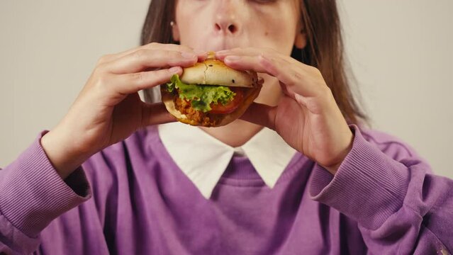 Young woman biting and eating chicken fat burger with bun, student eat beef burger close up.