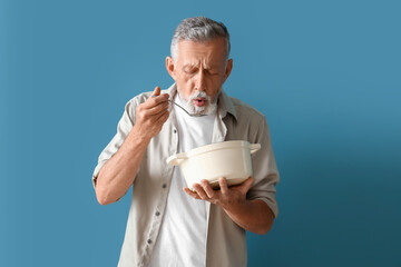 Mature man with spoon and cooking pot on blue background