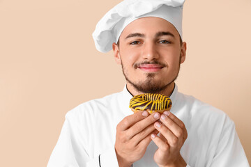 Male chef with tasty doughnut on beige background, closeup