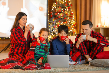 Happy family with cocoa watching Christmas movie on laptop at home
