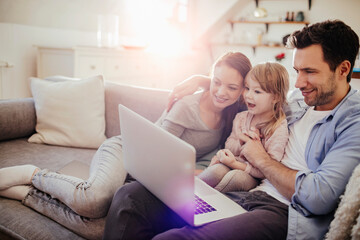 Young family looking at laptop on the couch at home