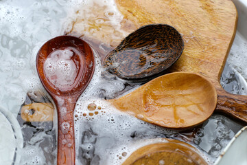 Wooden spoon, cutting board and dishes in water and bubbles of dishwashing liquid
