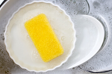 Dishes and bowls in water and bubbles of dishwashing liquid. Kitchen work