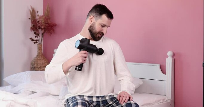 Man massaging his body with massage percussion device at home.