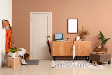 Interior of modern hallway with stylish autumn clothes, ottoman and wooden sideboard