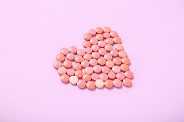 Heart made of pink pills on lilac background