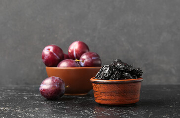 Bowls with tasty prunes and ripe plums on black grunge table