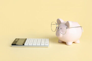 Piggy bank in eyeglasses with calculator on beige background