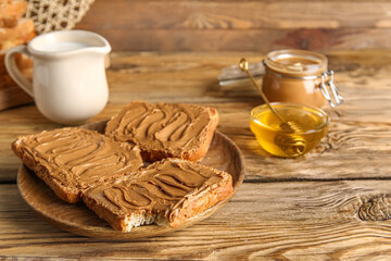 Plate of toasts with peanut butter and bowl of honey on wooden background