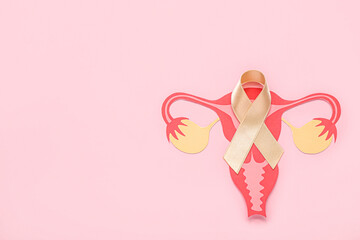 Paper uterus with beige ribbon on pink background. Cancer awareness concept