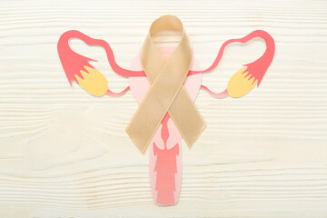 Beige ribbon with paper uterus on white wooden background. Cancer awareness concept