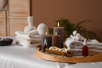 Burning candles with flowers and towels on couch in spa salon, closeup