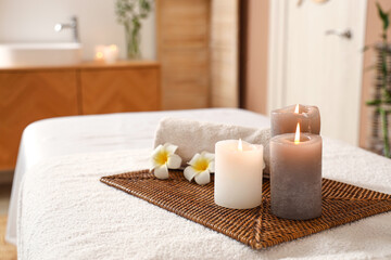 Fototapeta na wymiar Burning candles with flowers and towel on couch in spa salon, closeup