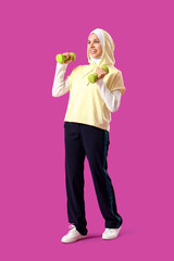 Sporty Muslim woman with dumbbells on purple background