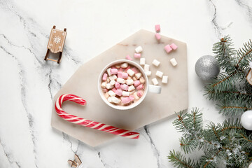 Cup of tasty Christmas cocoa with marshmallows, candy cane, balls and fir branches on white marble background