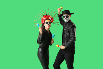 Young couple dressed for Mexico's Day of the Dead (El Dia de Muertos) with maracas on green background