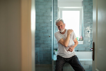 Senior man experiencing shoulder pain in the bathroom at home