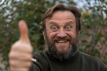 Portrait of cheerful optimist senior man looking at camera with thum up. Elderly bearded caucasian...