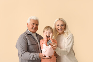 Obraz na płótnie Canvas Surprised little boy with his grandparents putting money in piggy bank on beige background