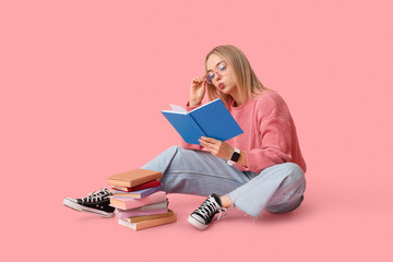 Beautiful young woman with many books sitting on pink background