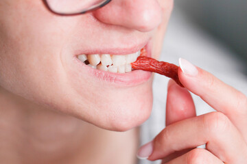Girl eating sausage. Woman eating meat snack. Mouth closeup. Thin dry smoked pork sausage. White teeth smile while eating. Food consumption background. - obrazy, fototapety, plakaty