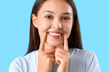 Fototapeta premium Smiling young Asian woman with healthy teeth on blue background, closeup