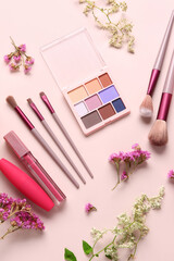 Composition with different cosmetic products, makeup brushes and flowers on pink background