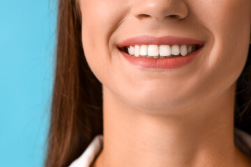 Fototapeta premium Smiling young woman with healthy teeth on blue background, closeup