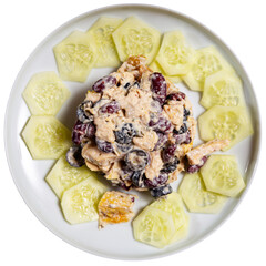 In center of plate is small portion of salad of chicken, olives, beans, seasoned with mayonnaise. Dish is decorated around edge of plate with round pieces of juicy cucumber. Isolated over white