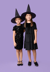 Cute little girls dressed for Halloween as witches on purple background