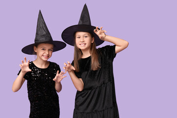 Cute little girls dressed for Halloween as witches on purple background