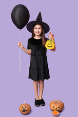 Cute little girl dressed for Halloween as witch with pumpkins, bag, balloon and candies on purple background