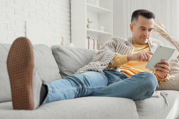 Handsome man with warm plaid using tablet computer at home