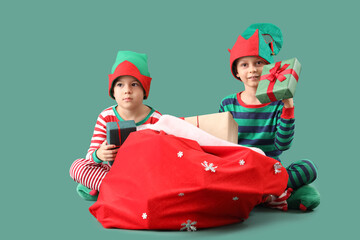 Cute little boys in elf costumes with bag of gifts on green background
