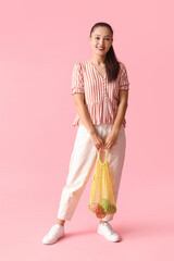 Young Asian woman holding strip bag with fresh apples on pink background