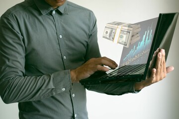 Hombre trabajando en su laptop. Analiza sus finanzas y ganancias viendo un gráfico de barras que sobresale de la pantalla  y un fajo de dólares billetes representan sus ganancias. - obrazy, fototapety, plakaty