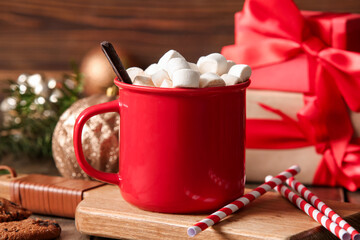Cup of hot cocoa with marshmallows and gift boxes on wooden background