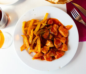 There is hot lunch on tablecloth of table. Juicy pork stew in sauce gravy with fried potato slices