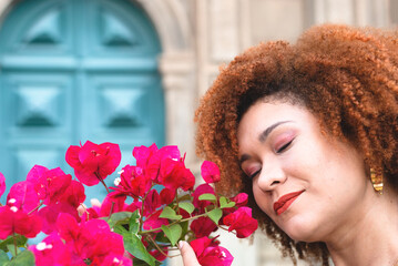 Naklejka premium Close-up portrait of a red-haired woman's face with her eyes closed smelling a flower close to her nose.