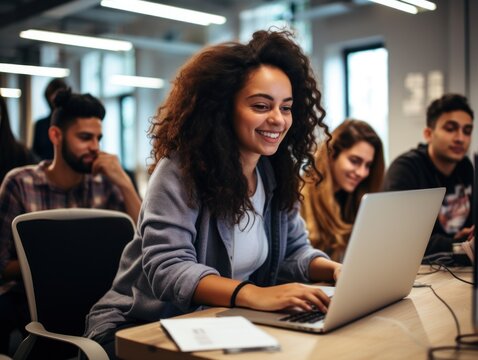 A joyful young woman with curly hair works on her laptop in a modern office setting, surrounded by focused colleagues.